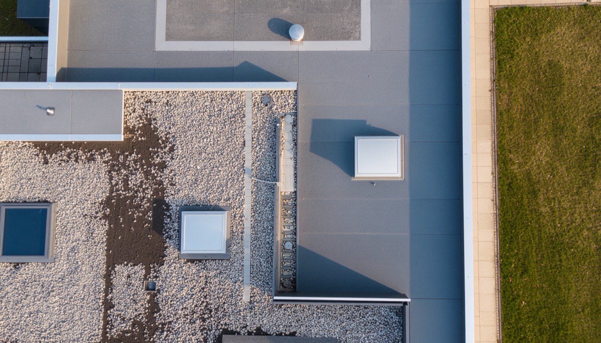Een plat dak recht van boven gezien, met dakbedekking, grind, lichtkoepels en een dakrand